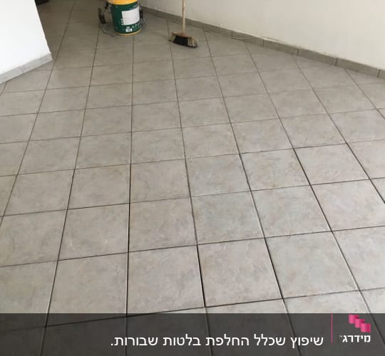 רצפה מרוצפת עם דלי צבע ומטאטא בפינה